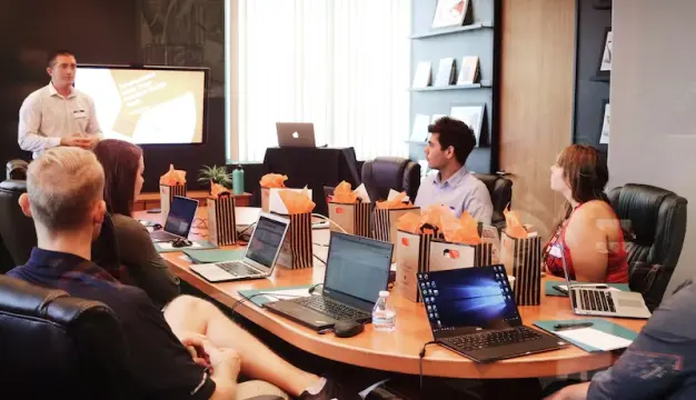 A presenter explaining a concept to a group of professionals with laptops.